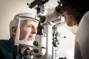 Optometrist giving eye exam to senior patient checking for age-related macular degeneration.